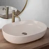 A beige matte washbasin with a brass faucet is shown on a wooden countertop, with a round mirror in the background. Produktbild-Vorschau
