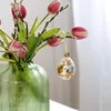 An Easter egg ornament hangs from a branch of tulips and pussy willows in a green vase. Produktbild-Vorschau