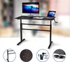 A black height-adjustable desk with a monitor and laptop on it, shown in a blurred office-like setting. Several close-up circular insets at the bottom show product details. Produktbild-Vorschau