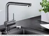 A modern kitchen faucet with a pull-out spray head is shown on a dark countertop next to a sink. A potted plant is visible in the background. Anteprima dell’immagine prodotto