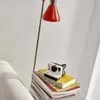 A vintage-style Polaroid camera sits on a stack of books next to a red desk lamp. Voir les images du produit