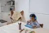 A young girl wearing headphones is using a tablet at a table. Produktbild-Vorschau