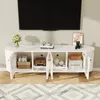 A white TV stand with open doors, displaying various items inside, with a large black TV mounted on the wall above it. Podgląd zdjęcia produktu