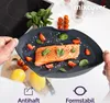 A close-up shot of a dark gray silicone baking dish with a piece of salmon, cherry tomatoes, and basil leaves on it. Two lemons and a knife are visible in the background. Produktbild-Vorschau