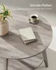 A round coffee table with a vase of flowers, a cup of coffee, and books on it. Produktbild-Vorschau