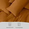 A close-up view of brown bedding with icons indicating washing and drying instructions. Náhled obrázku produktu