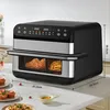 A black and silver air fryer oven is shown on a white countertop, with food inside and small plates of food in the foreground. Produktbild-Vorschau