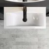 A top-down view of a white ceramic sink with a black faucet, set against a dark background and a tiled floor. Produktbild-Vorschau