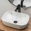 A white oval countertop sink with a marble pattern and a black faucet is shown on a wooden surface. Anteprima dell’immagine prodotto
