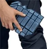 A hand is shown holding a blue knee pad over a pair of dark blue work pants. Produktbild-Vorschau
