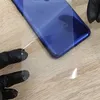 Hands in black gloves are holding a clear protective film over the back of a blue smartphone. Produktbild-Vorschau