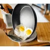 A person is using a spatula to slide fried eggs from a frying pan onto a plate. Náhled obrázku produktu