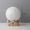 A white moon lamp sits on a wooden stand against a gray background. Produktbild-Vorschau
