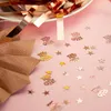 Close-up of rose gold confetti, including star shapes and text shapes, scattered on a pink surface. Produktbild-Vorschau