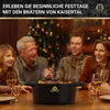 A family is gathered around a table, with a pot of food in the center, in a festive setting with a Christmas tree in the background. Produktbild-Vorschau