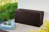 A brown storage box sits on a patio next to some plants. A tray with a lantern and berries is on a cushion in front of the box. Podgląd zdjęcia produktu