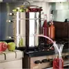 A stainless steel juicer is set up on a stove, with grapes in the top compartment and juice flowing into a glass carafe. Produktbild-Vorschau