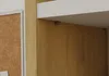 A close-up view of a shelf bracket on a wooden surface, with a corkboard visible on the left. Podgląd zdjęcia produktu