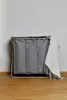 A laundry basket with a blanket draped over it, set against a plain wall and wooden floor. Produktbild-Vorschau