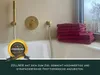 A bathroom scene with a bathtub, shower fixtures, and a stack of burgundy towels. Produktbild-Vorschau