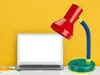 A desk lamp and a laptop are placed on a white surface against a yellow textured background. Produktbild-Vorschau