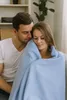 A couple is cuddling on a couch, wrapped in a light blue blanket. Produktbild-Vorschau