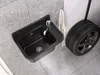 A black sink with a faucet is mounted on a tiled wall, next to a car tire. Produktbild-Vorschau
