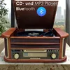 A vintage-style record player and stereo system is displayed on a marble countertop, with a blurred cityscape visible through a window in the background. Produktbild-Vorschau