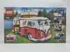 The image shows the packaging of a Lego VW T1 Campingbus model, set in a scenic outdoor environment with a lake and mountains. Podgląd zdjęcia produktu