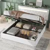 A white storage bed with its hydraulic lift mechanism open, revealing storage space filled with luggage and boxes. The bed has a tufted headboard with integrated LED lighting. Náhľad obrázku produktu