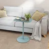 A small blue side table with a cup of coffee, a book, and a small plant on it, placed next to a light gray sofa with two pillows and a draped blanket. Náhled obrázku produktu