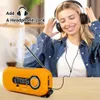 A woman is listening to music with headphones, with an orange emergency radio in the foreground. Produktbild-Vorschau
