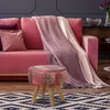 A pink sofa with a blanket and pillows, a patterned stool in the foreground, and a rug on the floor. Produktbild-Vorschau