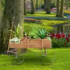 A wooden wagon planter filled with plants sits on a grassy lawn in a garden setting with a pond and flower beds in the background. Produktbild-Vorschau