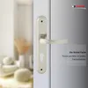 A close-up of a silver door handle and lock mechanism on a white door, with a blurred interior scene in the background. Produktbild-Vorschau