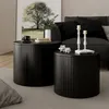 Two round black coffee tables with ribbed sides are placed on a gray rug in a living room setting. A painting of a tree hangs on the wall behind the tables, and a sofa with black cushions is visible in the background. Anteprima dell’immagine prodotto