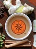 A cup of chai tea surrounded by spices like ginger, cinnamon sticks, star anise, nutmeg, and cardamom. Produktbild-Vorschau