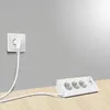 A white power strip with three outlets and USB ports sits on a wooden desk, connected to a wall outlet by a white cable. Produktbild-Vorschau