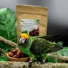 A parrot is perched on a branch next to a bowl of dates and a bag of parrot food. Voir les images du produit