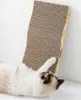 A cat is lying on its back next to a cardboard scratching board. Voir les images du produit