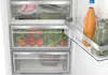 Close-up view of the inside of a refrigerator, showing drawers filled with fruits and vegetables, and a bottle of juice and a glass of iced drink on a shelf. Produktbild-Vorschau