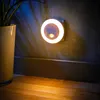 A night light with motion sensor plugged into a wall outlet, casting a warm glow on the wall and floor. Produktbild-Vorschau