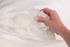 A hand is holding a handful of pillow filling over an open pillow. Náhled obrázku produktu