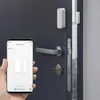 A hand holding a smartphone displaying a window sensor app, with a smart home window sensor attached to a door in the background. Anteprima dell’immagine prodotto