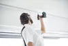 A person is using a cordless drill to screw something into a ceiling. Voir les images du produit