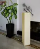 A tall, rectangular floor lamp with a beige paper shade stands next to a potted plant and a fireplace. Produktbild-Vorschau