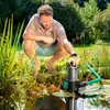 A man is crouching by a pond, holding a submersible pump. Produktbild-Vorschau