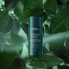 A bottle of Aveda Botanical Repair Bond-Building Pre-Shampoo Treatment is shown against a backdrop of green leaves and water droplets, with abstract green lines overlaying the image. Anteprima dell’immagine prodotto