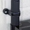 A close-up view of a black plastic bracket attached to a white brick wall, securing a black vertical pole. Produktbild-Vorschau