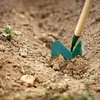 A close-up shot of a garden hoe digging into soil next to a small plant. Produktbild-Vorschau